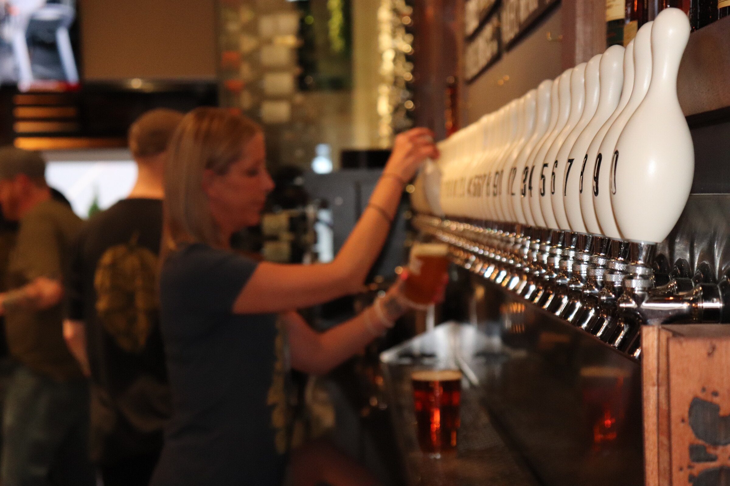 Bartender pouring a craft beer from the tap wall at Hoppinâ Vines
